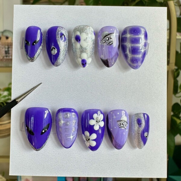 Custom press-on nail set featuring hand-painted alien and space-themed designs. Bright purple tones, glitter accents, florals, and extraterrestrial art on a short almond shape. Glossy finish and reusable nails for bold, statement-making looks.