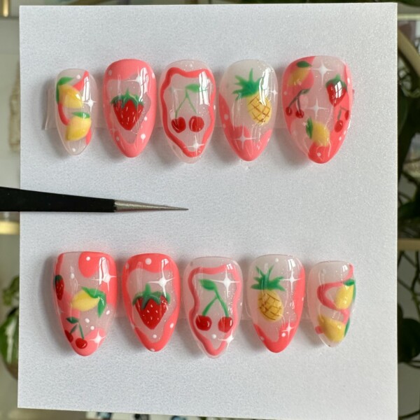 Hand-painted press-on nails with strawberries, cherries, pineapples, and lemons on soft pink and nude bases. Glossy finish with sparkles and fruit-themed swirls. Bright, playful summer nail set.