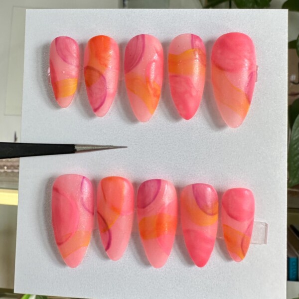 Freeform abstract swirls with layered watercolor effects in hot pink, tangerine, berry purple, and warm coral, creating a dreamy, sunset-inspired nail design.