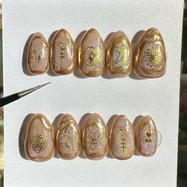 Cat-eye shimmer press-on nails with iridescent swirls, gold chrome floral decals, and a holographic finish. Soft, dreamy rainbow tones with a luxe, moonlit garden vibe.