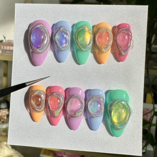 Mismatched pastel nail design featuring lavender, sky blue, mint green, peach, butter yellow, and bubblegum pink, each topped with a dimensional jelly gem and silver holographic halo. Glossy finish with a futuristic, candy-inspired, outer-space aesthetic.