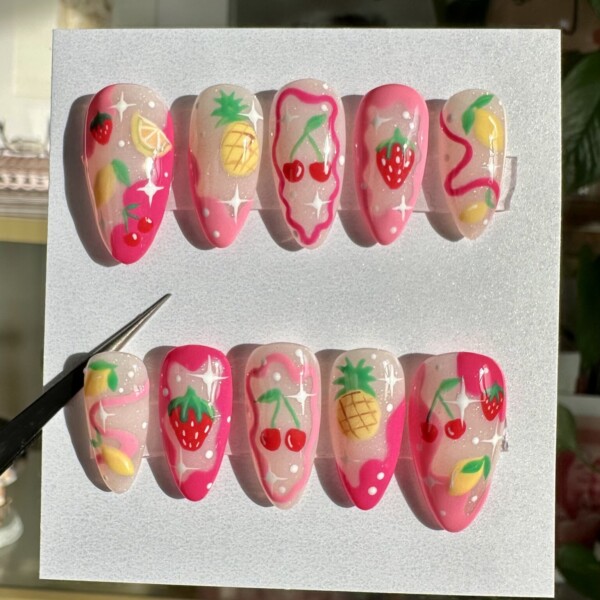 Hand-painted press-on nails with strawberries, cherries, pineapples, and lemons on soft pink and nude bases. Glossy finish with sparkles and fruit-themed swirls. Bright, playful summer nail set.