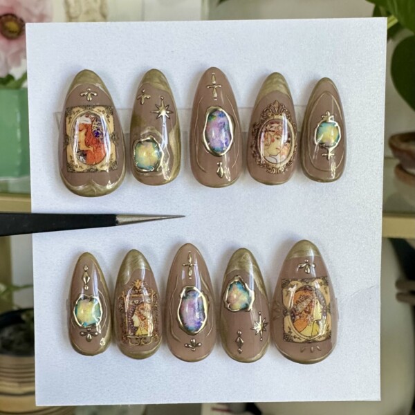 Art Nouveau-inspired press-on nails with taupe and gold marble, iridescent gems, and vintage-style portrait decals. Glossy finish with ornate, hand-painted details for an elegant, gallery-worthy look.