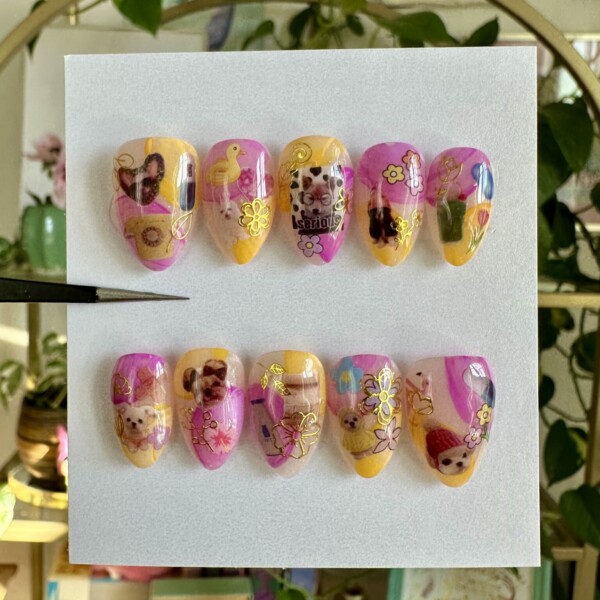 Collage-style nail design with dog stickers, tiny florals, hearts, telephones, milkshakes, and playful icons layered over a nude base. Features neon purple, golden orange, gold foil, and multicolor accents for a vibrant, sticker-inspired look.