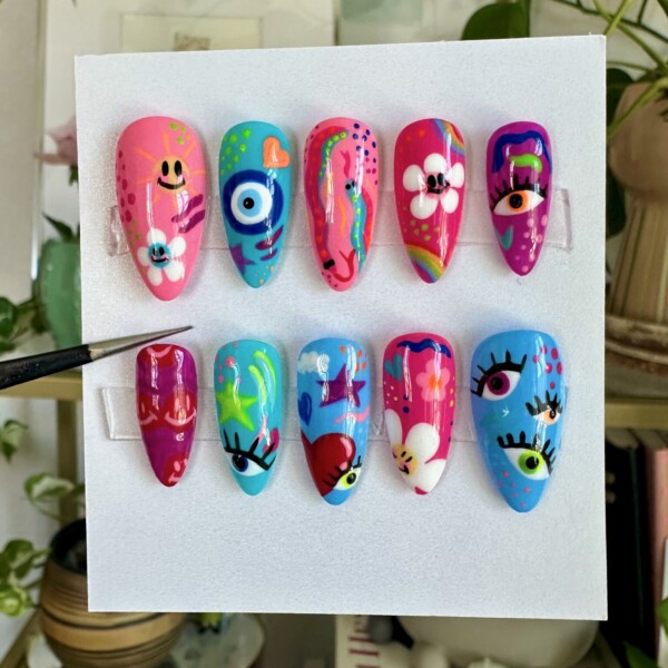 Bright and colorful hand-painted press-on nails featuring abstract designs, eyes, florals, and playful patterns. Medium almond shape with a glossy finish. Unique and artsy nail art perfect for bold self-expression. Custom, reusable, and handmade press-on nail set.