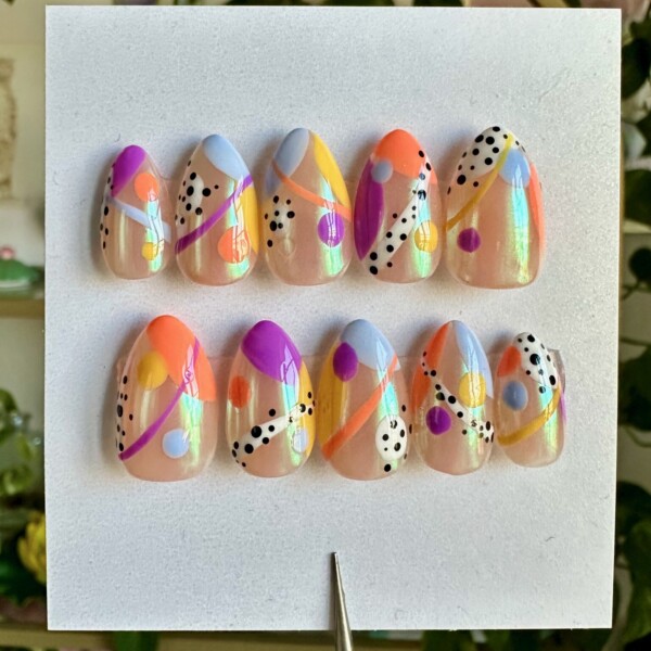 Short almond press-on nails with a pearl shimmer base featuring abstract Kandinsky-inspired designs in orange, purple, yellow, blue, and black dots. Each nail has a unique composition of bold curves, circles, and playful patterns.