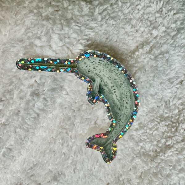 Glitter sticker of a green-gray narwhal with a long spiraled tusk, surrounded by sparkling rainbow edges.