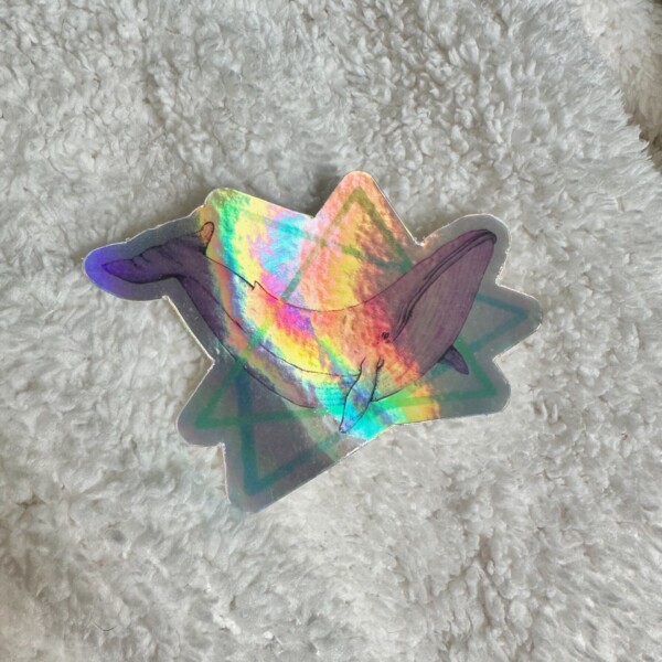 Holographic sticker featuring a pink watercolor blue whale surrounded by teal and blue geometric triangles in a retro 80s style.